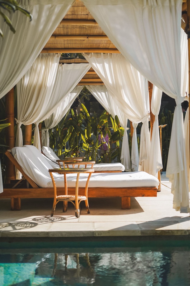 White curtained cabana with loungers beside a pool
